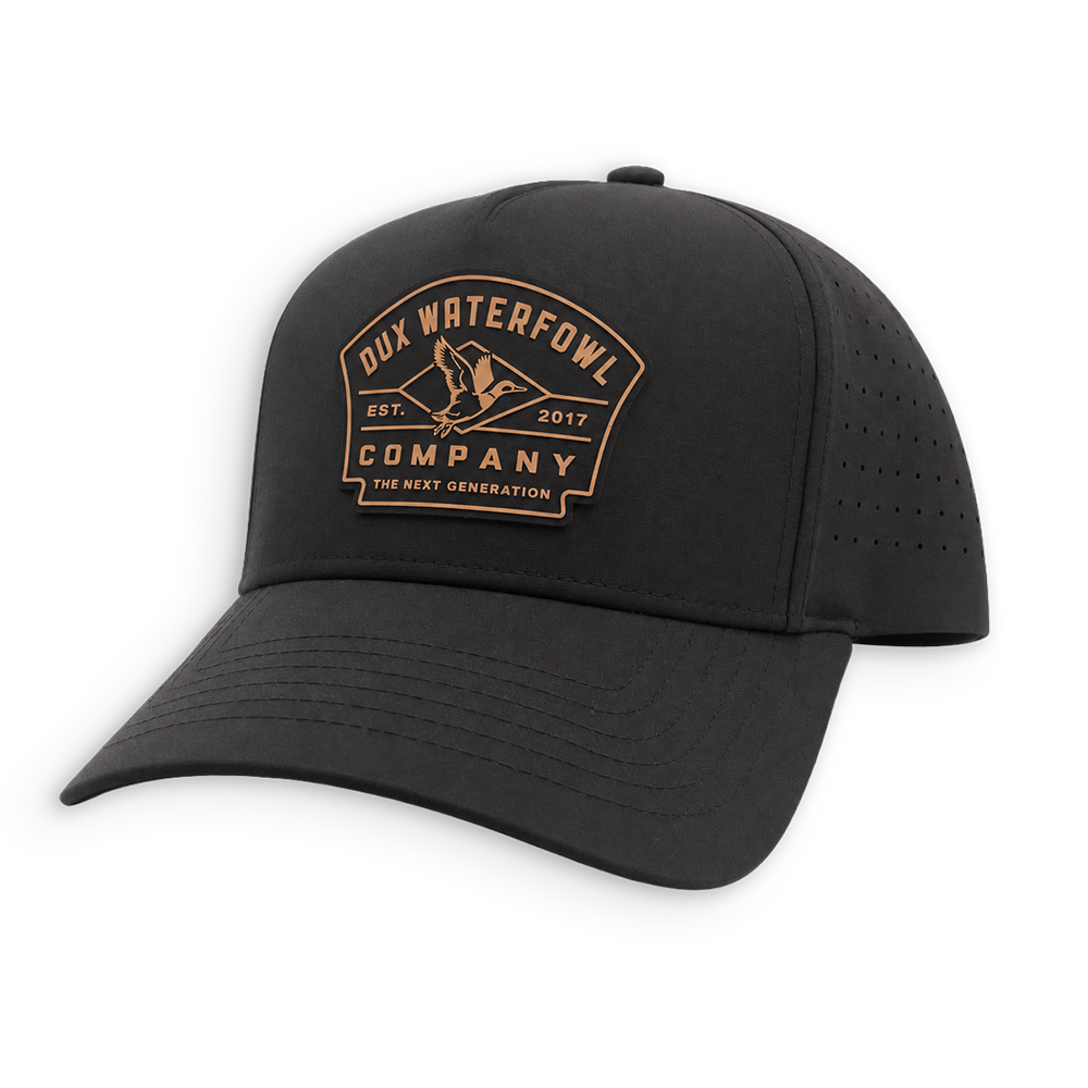 A black hat with a curved brim, featuring a tan embroidered logo on the front that reads 'Dux Waterfowl Company' with a duck silhouette. The cap has perforated side panels for ventilation and is shown against a plain white background.