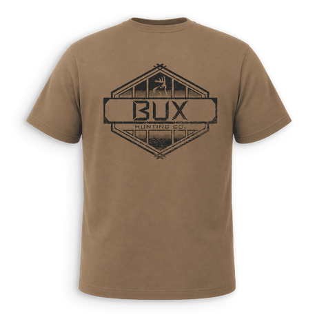 Back of tan crewneck t-shirt with black trim on the collar and sleeve cuffs, featuring a small black line-art deer logo on the left chest, displayed against a solid green background.
