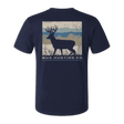 A navy blue short-sleeve t-shirt with a back graphic showing a deer silhouette over a rustic landscape and the text 'BUX HUNTING CO.' in white, displayed against a solid green background.