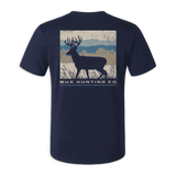 A navy blue short-sleeve t-shirt with a back graphic showing a deer silhouette over a rustic landscape and the text 'BUX HUNTING CO.' in white, displayed against a solid green background.