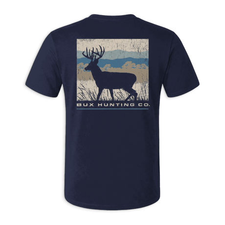 A navy blue short-sleeve t-shirt with a back graphic showing a deer silhouette over a rustic landscape and the text 'BUX HUNTING CO.' in white, displayed against a solid green background.