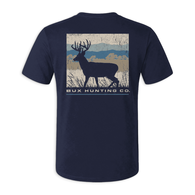 A navy blue short-sleeve t-shirt with a back graphic showing a deer silhouette over a rustic landscape and the text 'BUX HUNTING CO.' in white, displayed against a solid green background.