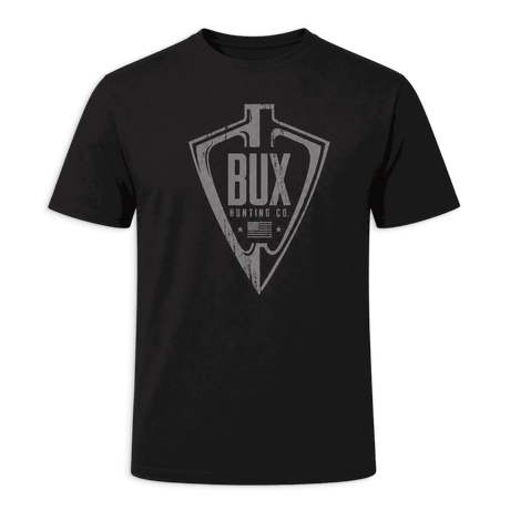 A black short-sleeve crewneck t-shirt featuring a distressed gray graphic on the chest with an arrowhead and the text 'BUX HUNTING CO'. The shirt is displayed against a solid dark green background.