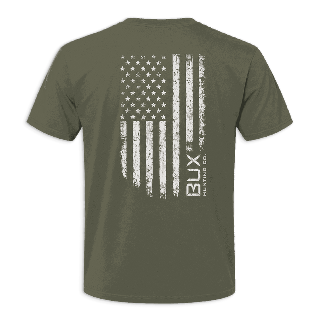 An olive green short-sleeve t-shirt shown from the back, featuring a distressed white American flag graphic with the vertical text 'BUX manufacturing CO.' printed on the right side of the flag.