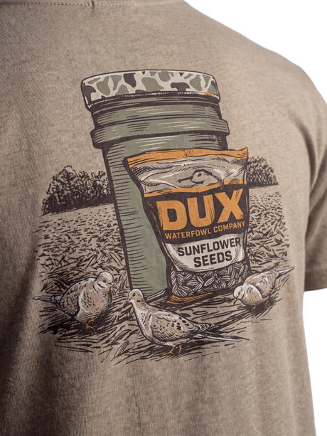Close-up of a heather taupe t-shirt featuring a graphic print of a Dux Waterfowl Company sunflower seed jar and bag with three doves on a field background.