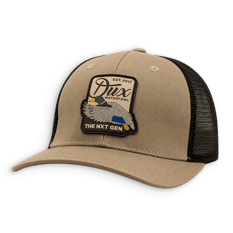 A tan and black trucker hat with a black mesh back and a large embroidered patch on the front. The patch features an eagle and the text 'Dux Waterfowl' and 'The Next Gen'.