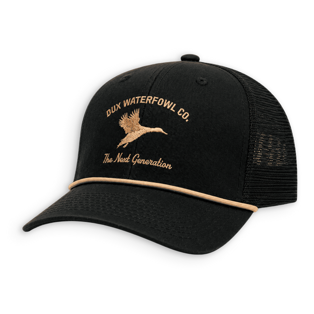 A black trucker hat with a curved brim, black mesh back, and tan embroidered logo and text reading 'DUX WATERFOWL CO.' and 'The Next Generation' on the front panel.