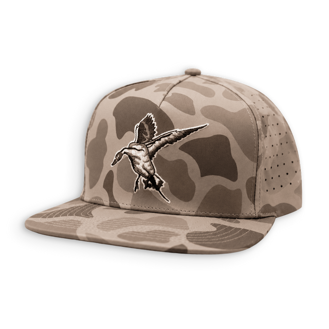 A flat-brim snapback cap in a desert camouflage pattern, featuring a detailed embroidered duck hunting duck on the front panel. The cap has a tan and brown camo pattern with a matching flat brim and perforated side panels.