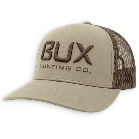 A khaki beige trucker hat with dark brown mesh back panels and dark brown embroidered 'BUX HUNTING CO.' branding on the front, shown on a plain white background.
