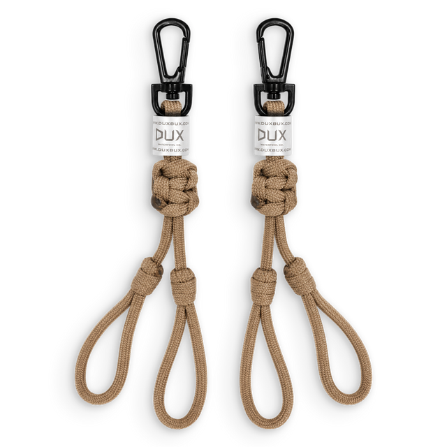 Two tan paracord keychains with black carabiners and white DUX brand labels, displayed side-by-side on a white background.
