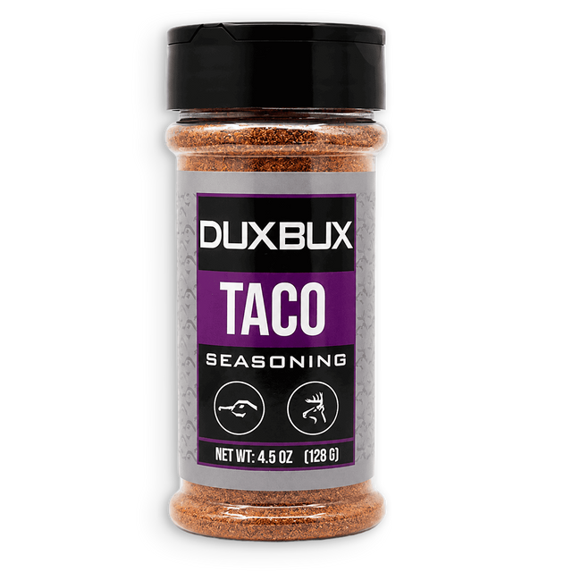 A bottle of Duxbux Taco Seasoning with a black cap and a gray and purple label, filled with brown seasoning, on a white background.